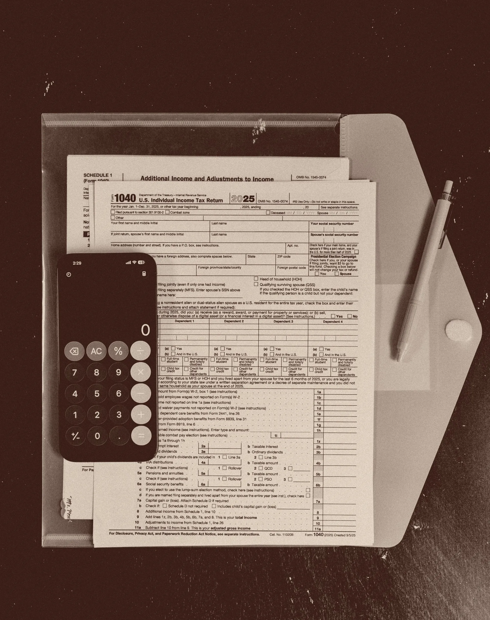 Overhead view of a blank 2025 Form 1040 and its Schedule 1, Additional Income and Adjustments to Income, fanned out on a manila folder on a dark desk, with a mechanical pencil beside them and a phone showing an open calculator resting on the page.