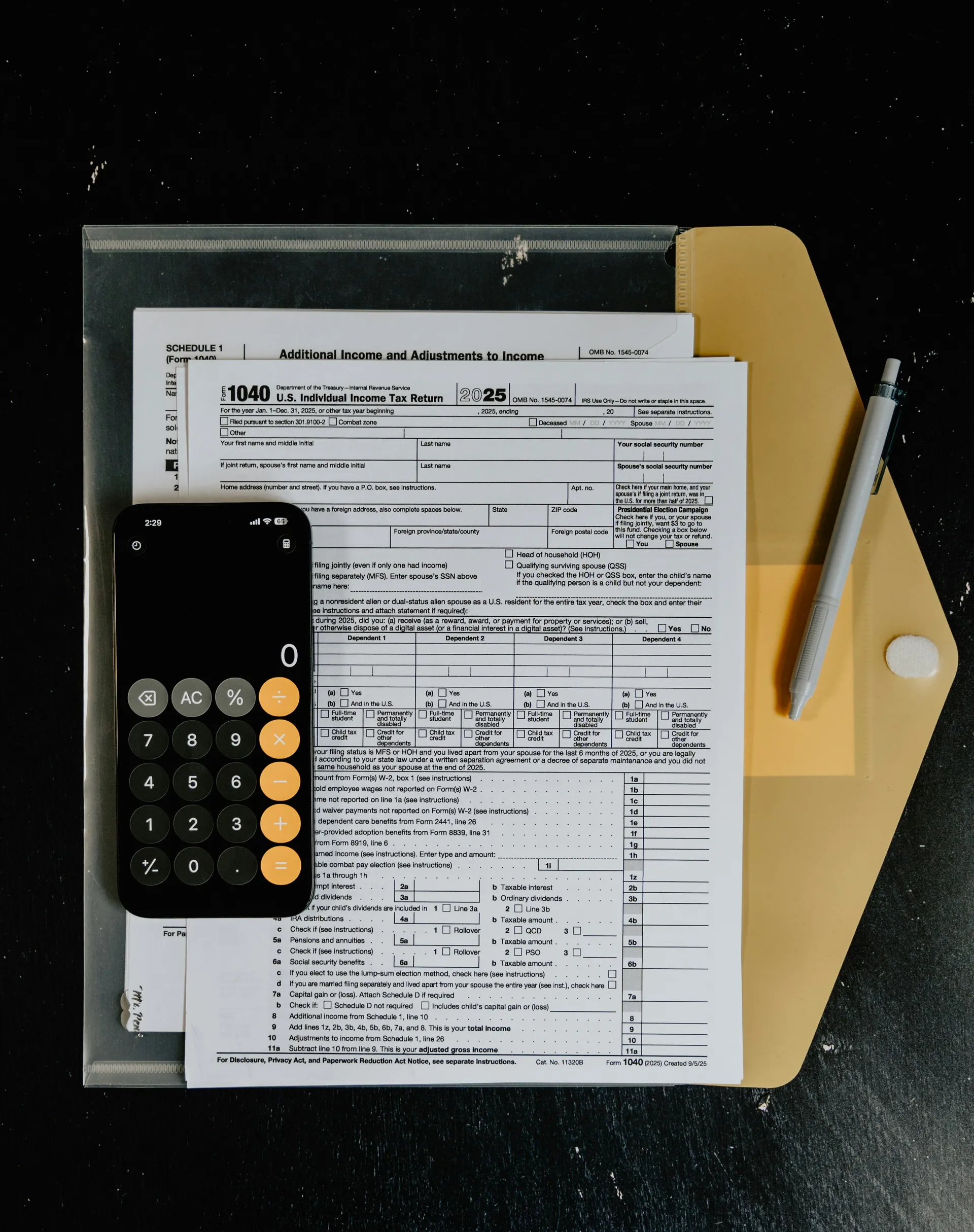 Overhead view of a blank 2025 Form 1040 and its Schedule 1, Additional Income and Adjustments to Income, fanned out on a manila folder on a dark desk, with a mechanical pencil beside them and a phone showing an open calculator resting on the page.